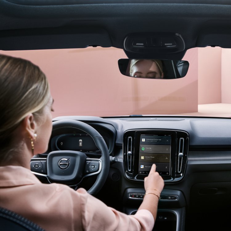 Woman seen from the back sitting in the drivers seat while interacting with a Volvo car’s infotainment system.